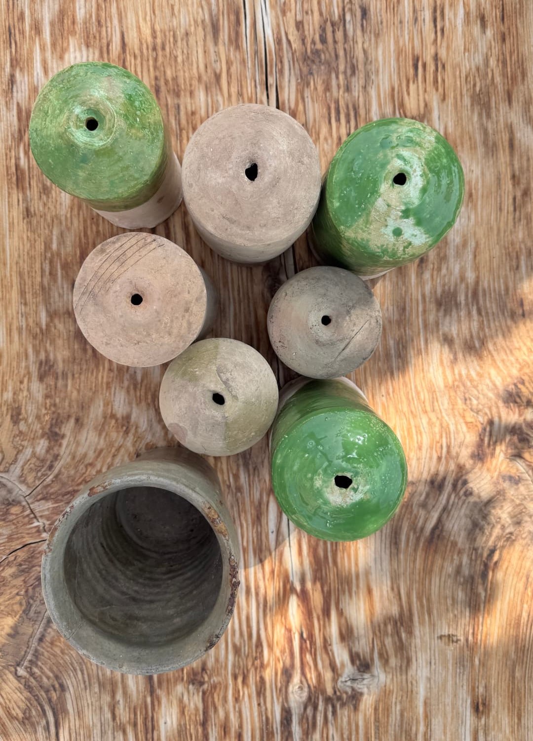 Green-glazed and raw ceramic vessels on a wooden table