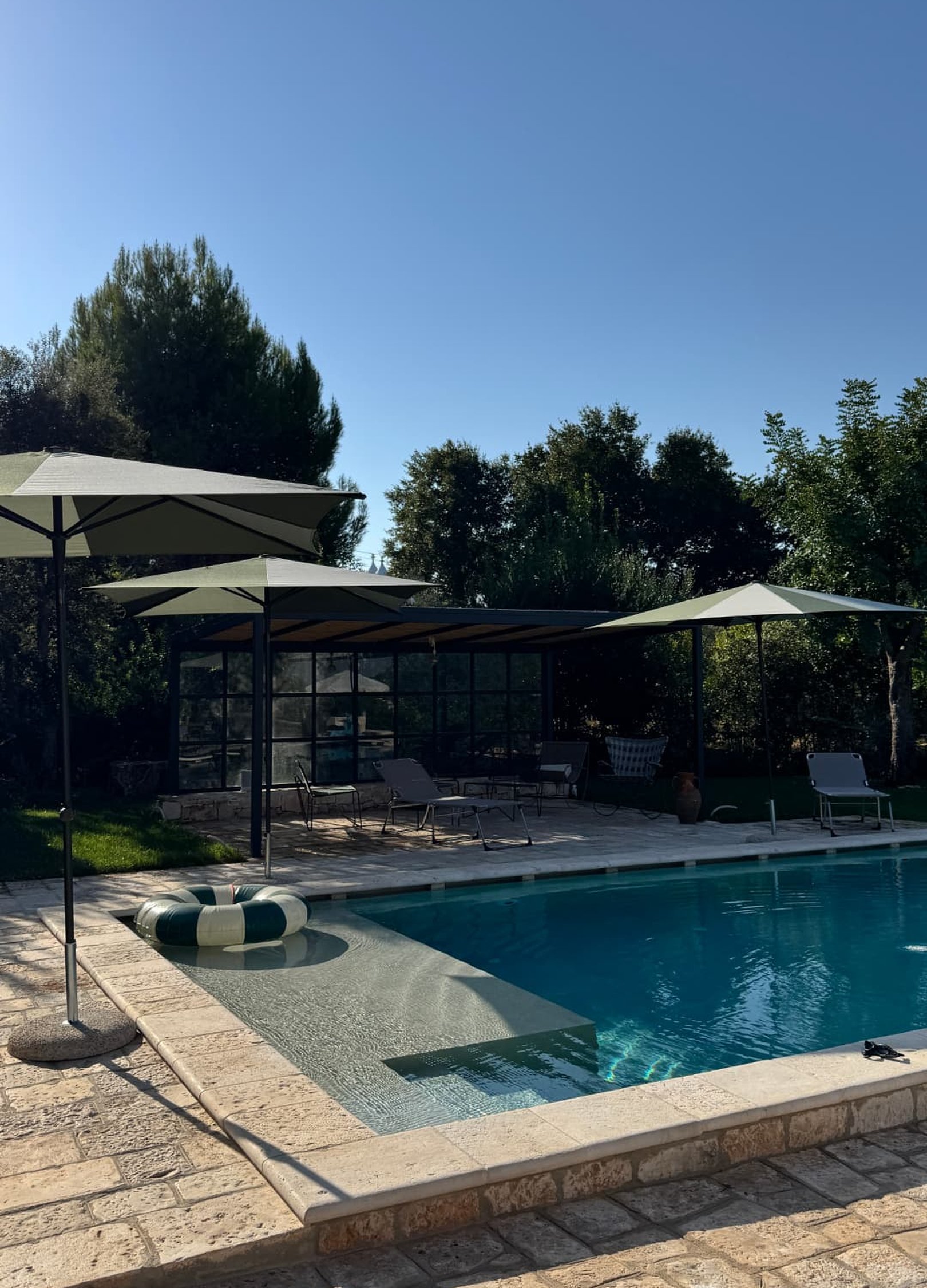 Green parasols over loungers by the pool and a glass pavilion